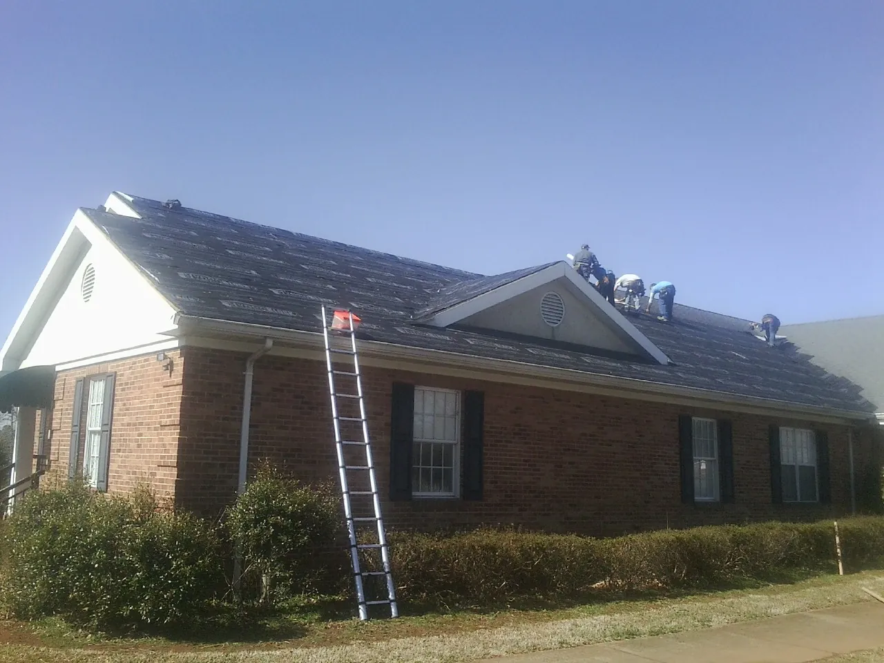 Crew tearing shingles off a brick ranch roof with a ladder set — Emergency Roof Repair work by our crew in Leighton