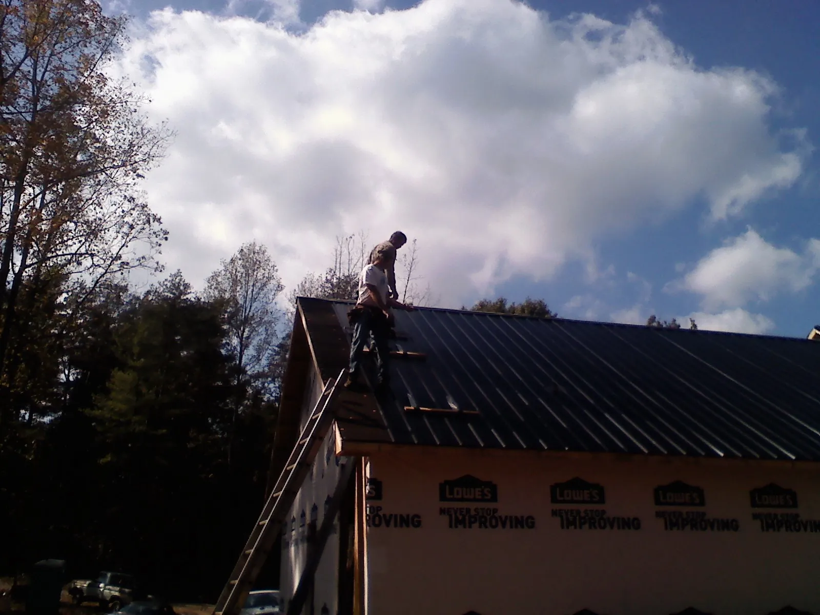 Roofer fastening dark metal panels high against a cloudy sky, from a Roof Inspection job in Leighton