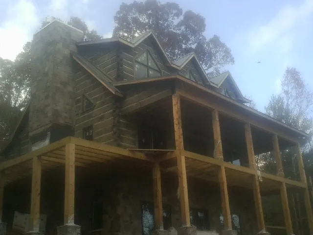 Stone chimney and dormers on a large log home with a timber porch in Leighton